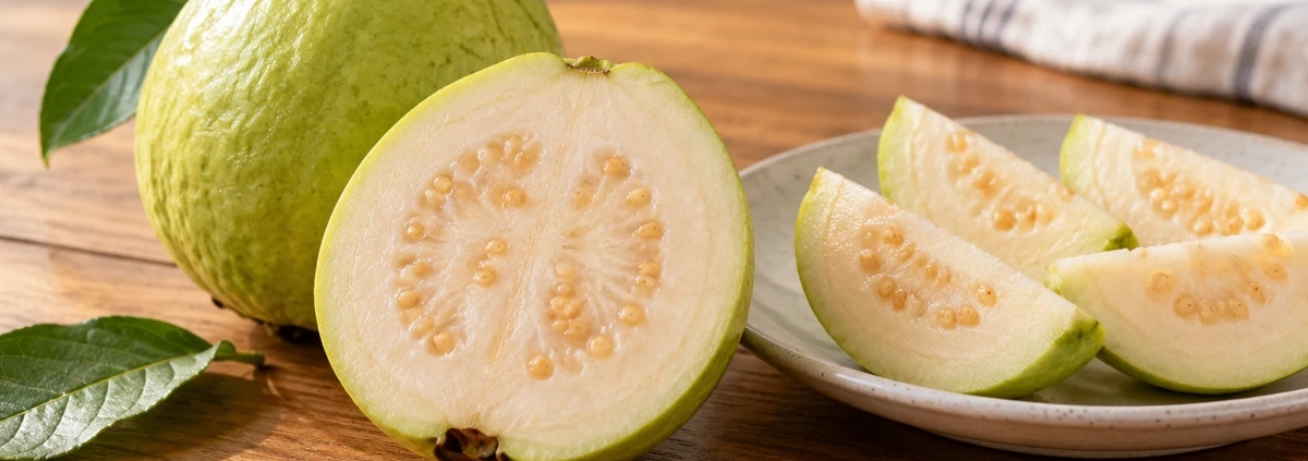 เตรียมฝรั่งเป็นของว่างให้สะดวก: จากผลสดสู่กล่องพร้อมกินอย่างพอดี 1 ผลฝรั่งทั้งผลและฝรั่งผ่าครึ่งข้างจานชิ้นฝรั่งบนโต๊ะไม้
