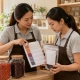 ทำ Product Knowledge Card ผลไม้แห้งสำหรับพนักงานใหม่: ตอบจากฉลาก ไม่เดาสรรพคุณ 3 พนักงานผู้ใหญ่สองคนตรวจการ์ดข้อมูลเทียบกับถุงผลไม้แห้ง